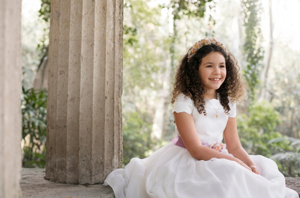 ein kleines lächelndes Mädchen in einem weißen Kleid, das sich auf seine Erstkommunion vorbereitet