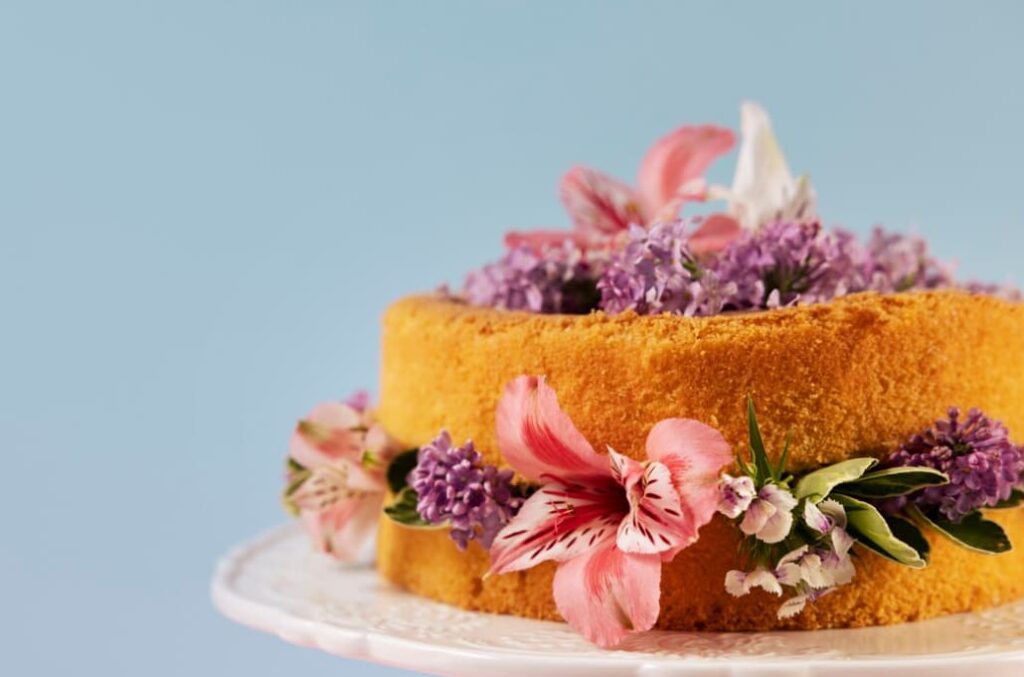 Ein Biskuitkuchen mit rosa und lavendelfarbenen Blüten auf einem weißen Teller